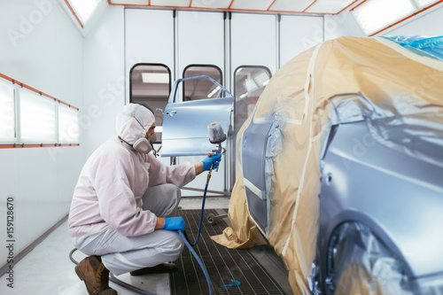 Schilderij op canvas Man with protective clothes and mask painting car using spray compressor