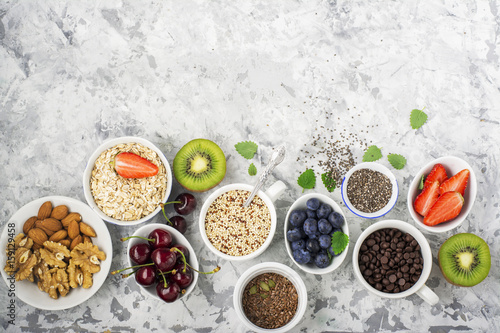 Healthy fitness food from fresh fruits, berries, greens, super food: kinoa, chia seeds, flax seed, strawberry, blueberry, kiwi, cherry, almonds, walnuts, mint, oatmeal natural flakes on a light marble
