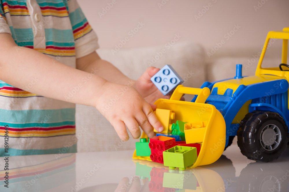Closeup of toddler boy's hands playing with colorful toy tractor. Child playing with a car at a nursery or preschool.