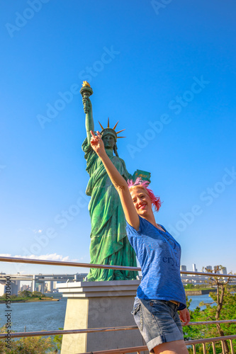 Happy tourist woman enjoying indicating Statue of Liberty, icons of Odaiba Island in Tokyo, Japan. Female lifestyle smiling while on a trip out of Tokyo in popular Odaiba. Summer vacation in Japan.