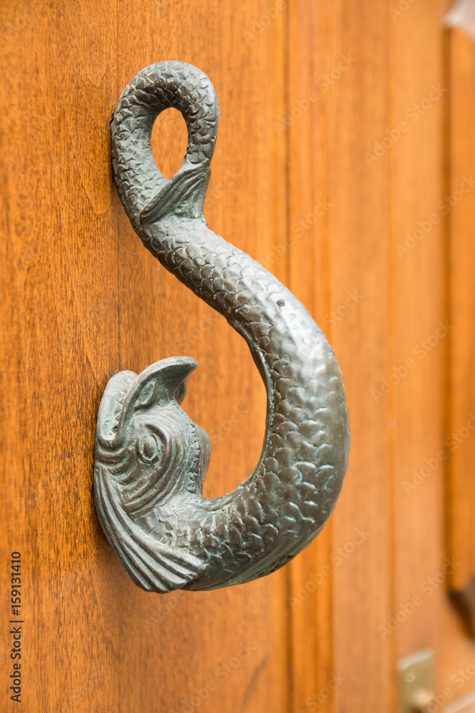 Old wooden door with a brass knocker in the shape of a fish Old wooden door with a brass knocker in the shape of a fish