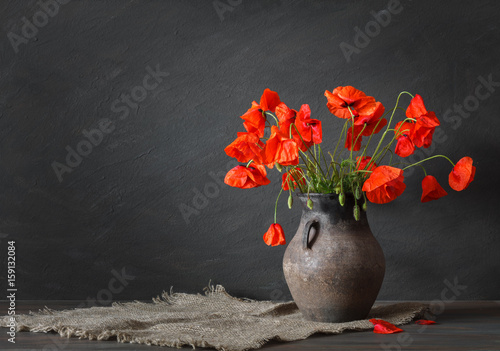 Still life in a rustic style: an old crock and a bouquet of red poppies on a wooden table