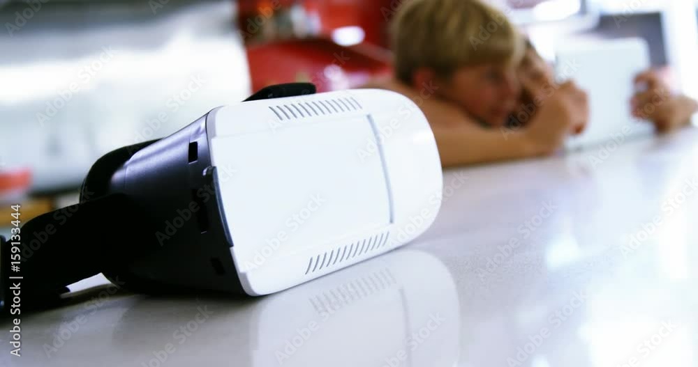 Close-up of virtual reality headset on kitchen worktop while siblings using digital tablet Close-up of virtual reality headset on kitchen worktop while siblings using digital tablet