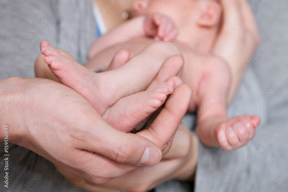 The hands of the father hold the legs of the newborn son The hands of the father hold the legs of the newborn son