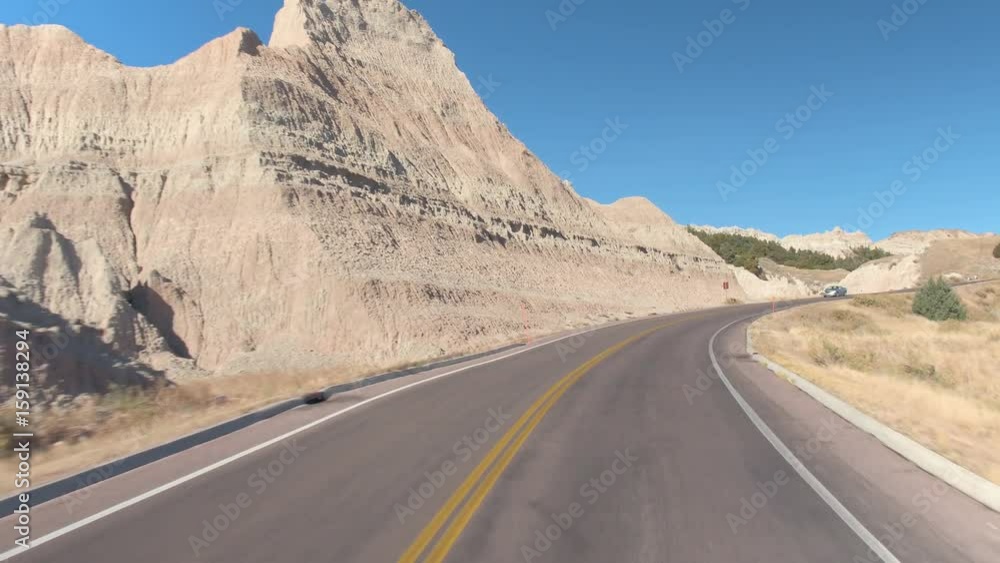 FPV: Driving along the empty road winding through stunning Badlands landscape with rocky sandstone formations. Traveling across the Badlands desert in South Dakota. Road trip across United States. FPV: Driving along the empty road winding through stunning Badlands landscape with rocky sandstone formations. Traveling across the Badlands desert in South Dakota. Road trip across United States.