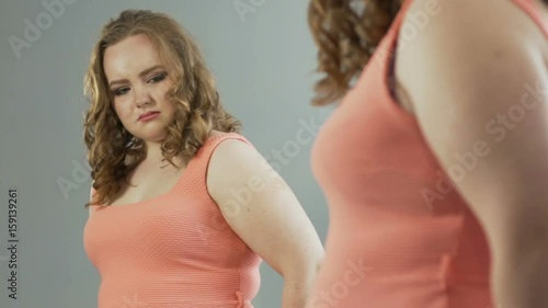 Female with extra weight looking at her reflection in mirror with self-loathing
