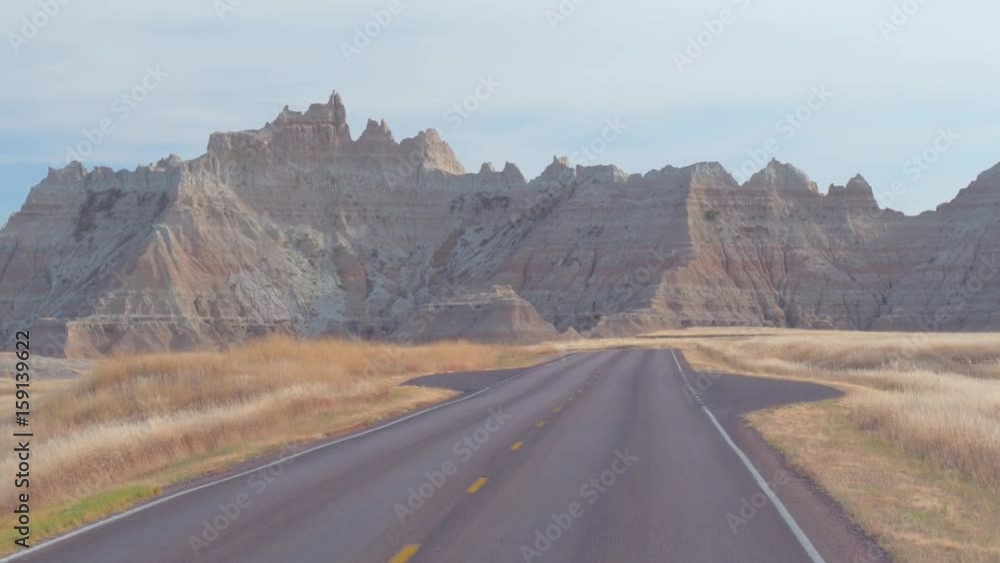 FPV: Driving along the empty road towards the picturesque Badlands landscape with rocky sandstone formations. Traveling across the Badlands desert in South Dakota. Road trip across United States. FPV: Driving along the empty road towards the picturesque Badlands landscape with rocky sandstone formations. Traveling across the Badlands desert in South Dakota. Road trip across United States.