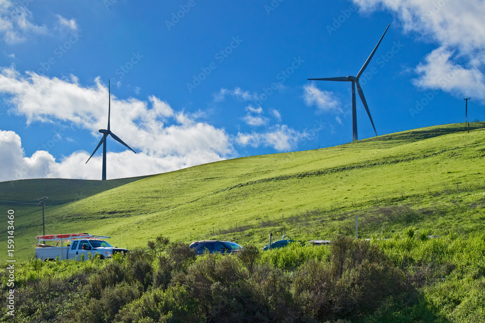 Two wind turbines on a hillside, against the backdrop of cloud-filled blue sky in the Livermore, California wind farm Two wind turbines on a hillside, against the backdrop of cloud-filled blue sky in the Livermore, California wind farm