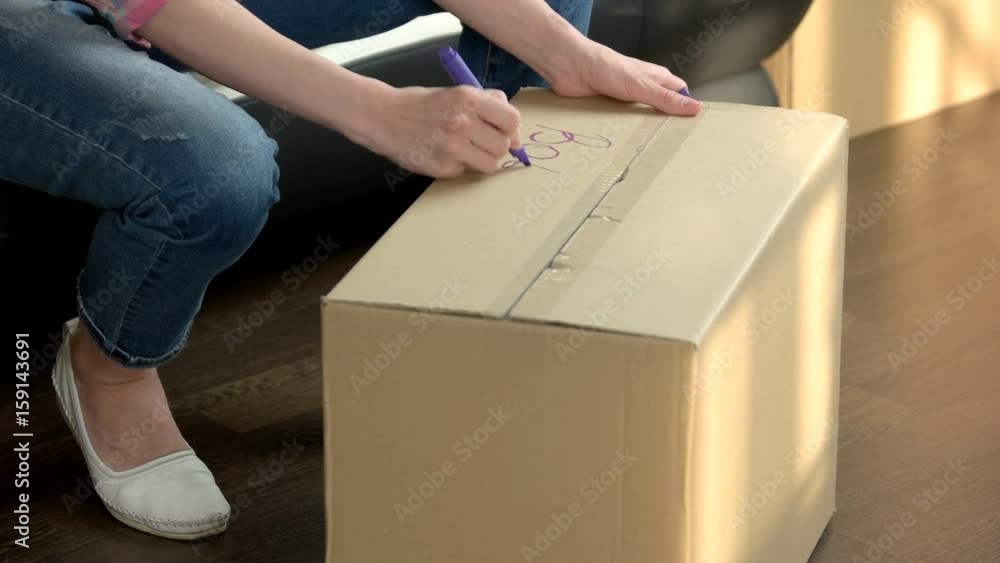 Hand writing on cardboard box. Woman picking up box. Hand writing on cardboard box. Woman picking up box.