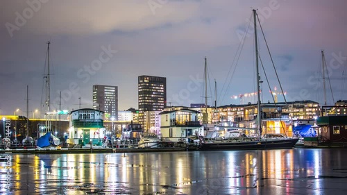 Small harbor at night 4K Time Lapse. Houseboat and sailboat marina, reflections on the ice, office buildings in the background photo