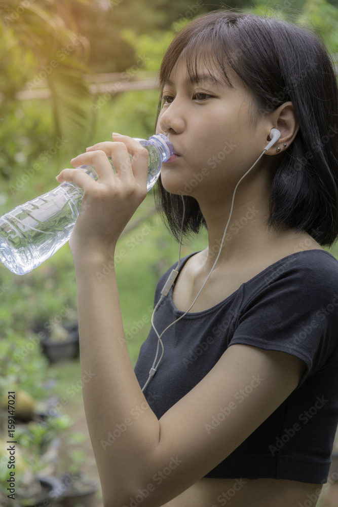 Smiling female model holding transparent bottle water in her hand and drinking water.