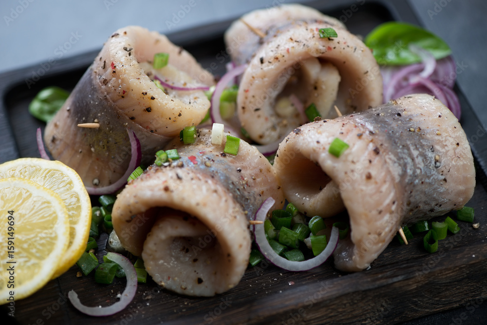 Herring fillet rolls with red and green onion, spices and lemon, close-up, selective focus Herring fillet rolls with red and green onion, spices and lemon, close-up, selective focus