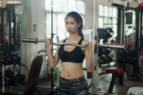 Athletic young asian woman in sportswear performing barbell exercise in gym