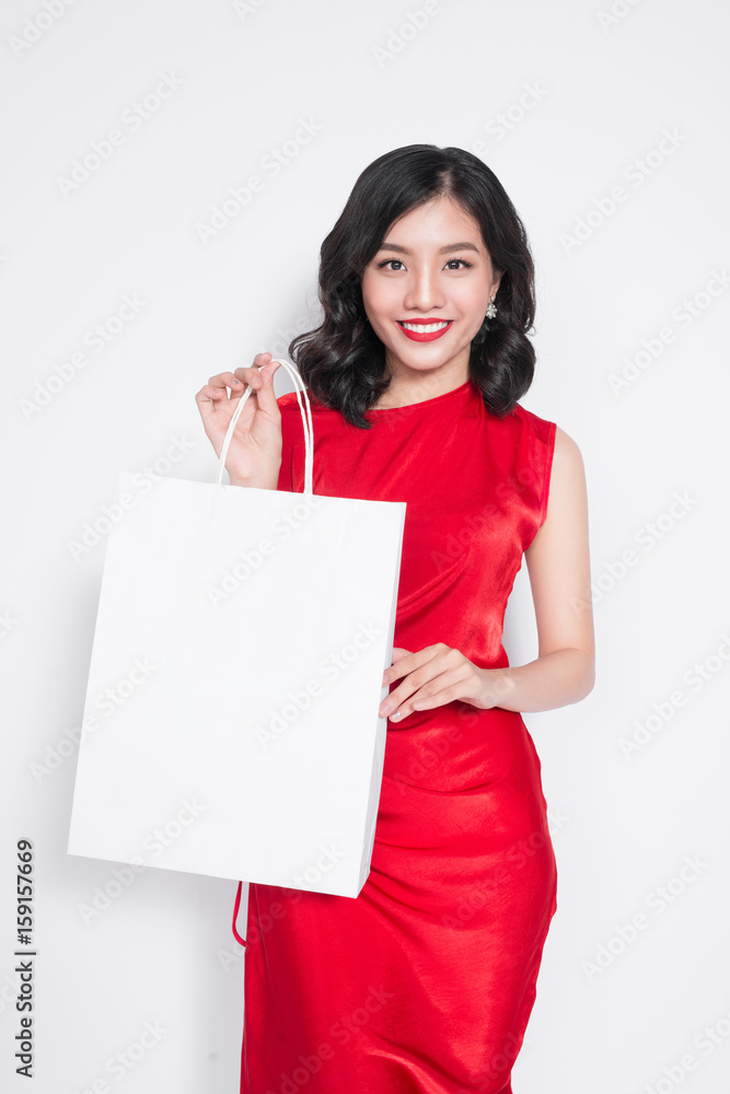 Beautiful asian woman wearing a red dress with shopping bag standing over white. Beautiful asian woman wearing a red dress with shopping bag standing over white.