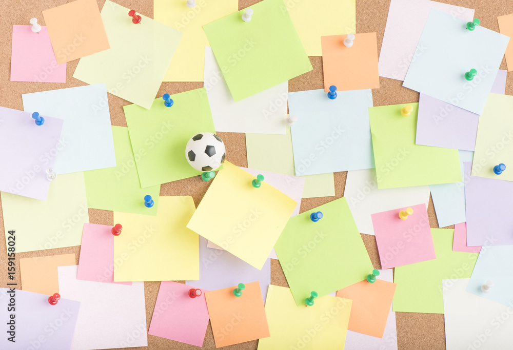 Football or soccer ball and blank sticky notes on notice board in office. Concept image of business related sport and leisure. Reminder of summer vacation and games. Football or soccer ball and blank sticky notes on notice board in office. Concept image of business related sport and leisure. Reminder of summer vacation and games.