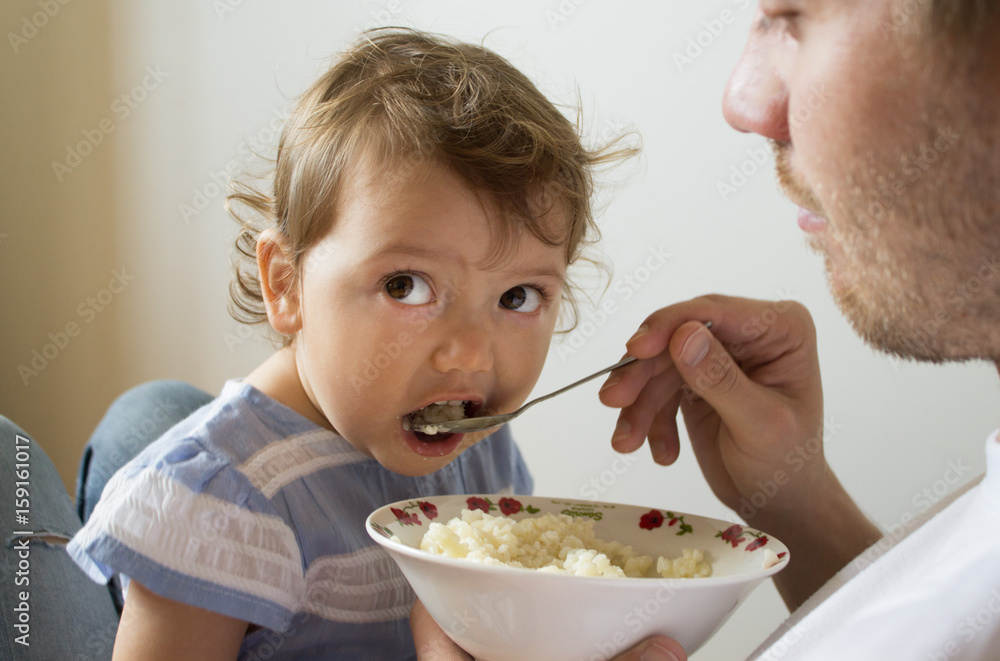Dad feeds the baby porridge. The child does not want to eat porridge. Young father Dad feeds the baby porridge. The child does not want to eat porridge. Young father