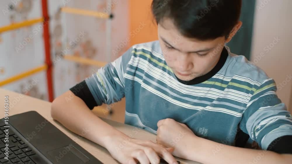 Boy-teenager at the computer table enthusiastically typing SMS on the smartphone Boy-teenager at the computer table enthusiastically typing SMS on the smartphone