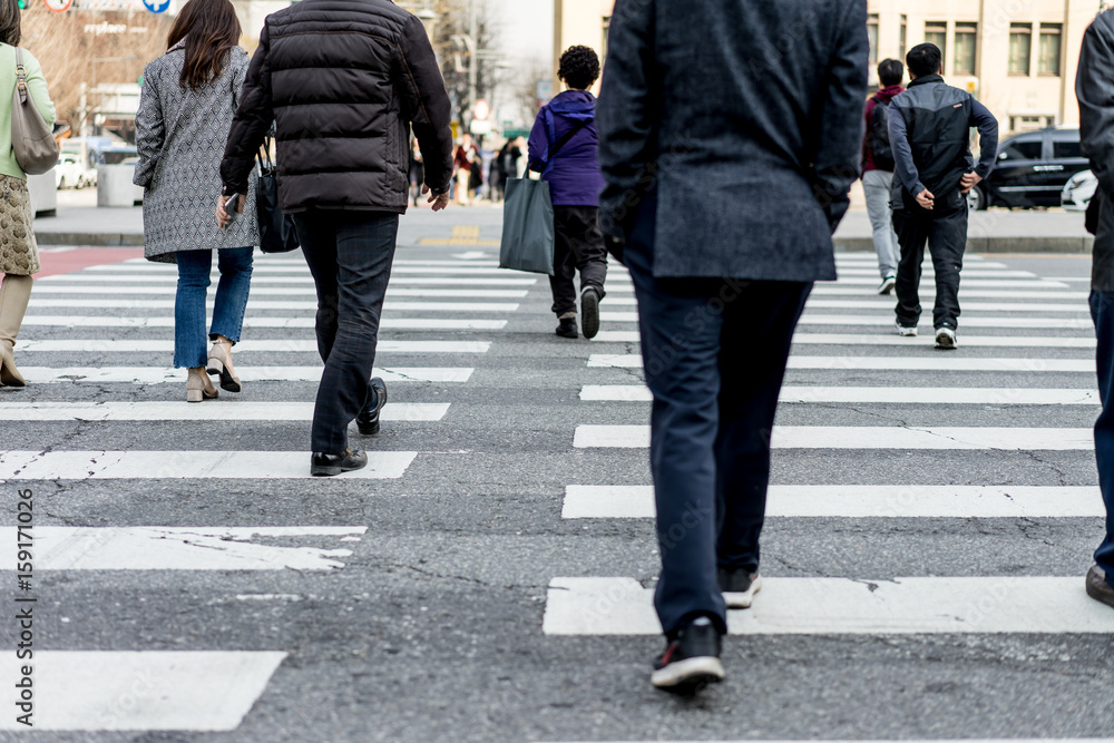 People are walking on a crosswalk on a city street.