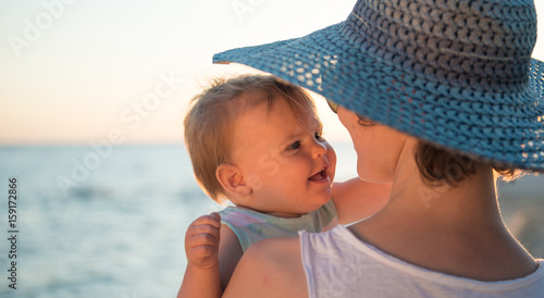 Mother with hat embracing little dougter at beach photo