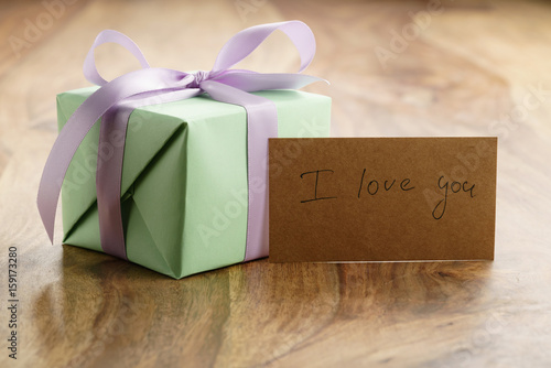 green paper gift box with purple ribbon bow on old wood table with i love you paper card, shallow focus