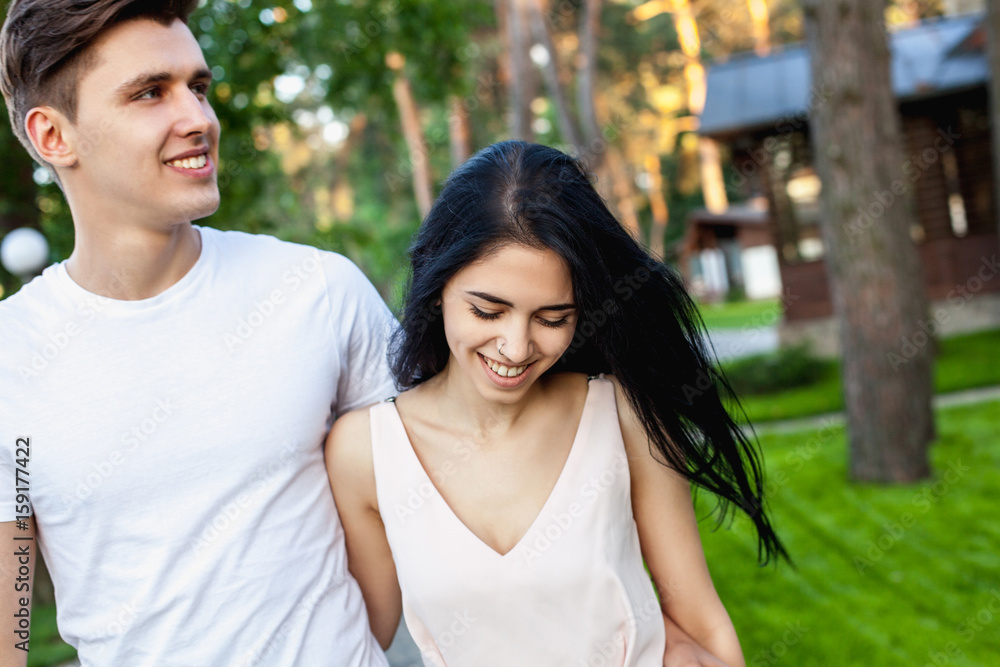 The guy hugs the waist of the girl with a shy smile while walking in nature. Beautiful young couple during a romantic date. The guy hugs the waist of the girl with a shy smile while walking in nature. Beautiful young couple during a romantic date.
