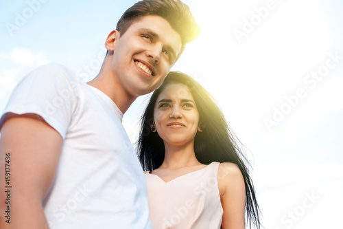 The guy and the girl with the perfect smile, laugh and look forward in the background of a Sunny day. Beautiful young couple during a romantic date. © mikhail_kayl