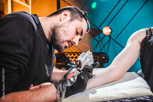master tattooist makes a tattoo on the skin of the hand client girl in a workshop with special equipment