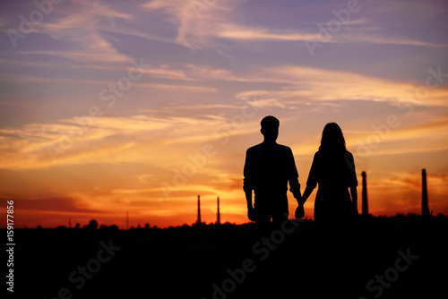 young couple is holding hands on a background sunset silhouette