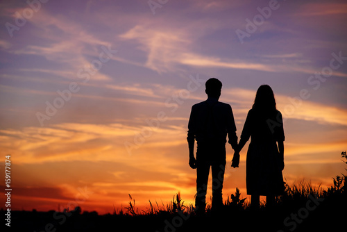 young couple is holding hands on a background sunset silhouette © cezarksv