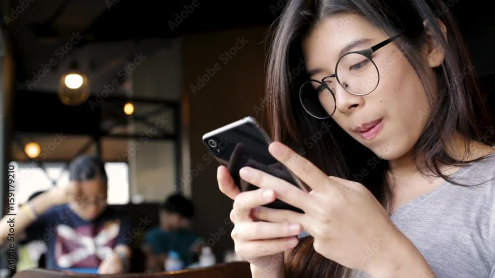 Close up young asian woman wear eyeglasses using cell phone connect social online in restaurant Close up young asian woman wear eyeglasses using cell phone connect social online in restaurant