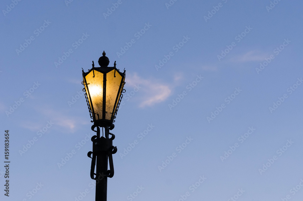 Glowing street lamp against a blue sky.