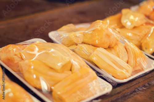 Jackfruit (Artocarpus heterophyllus) wrapped with plastic cover for display for sale on a wooden table market stall.