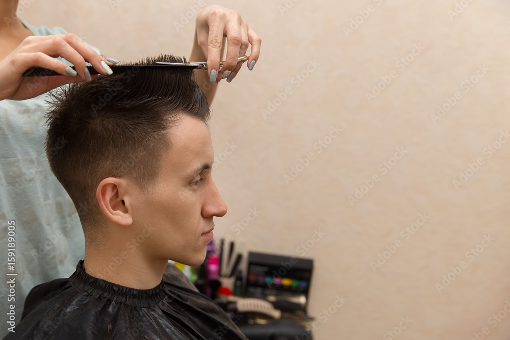 Fototapeta premium Side view of young man getting groomed at hairdresser while sitting in chair at barbershop.