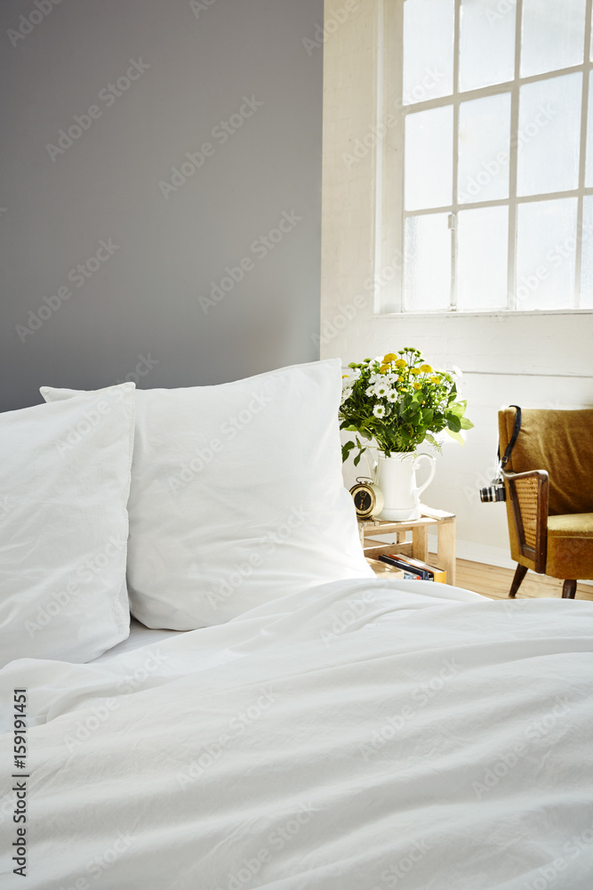 Fototapeta premium white bed linen fresh flowers on night stand industrial loft