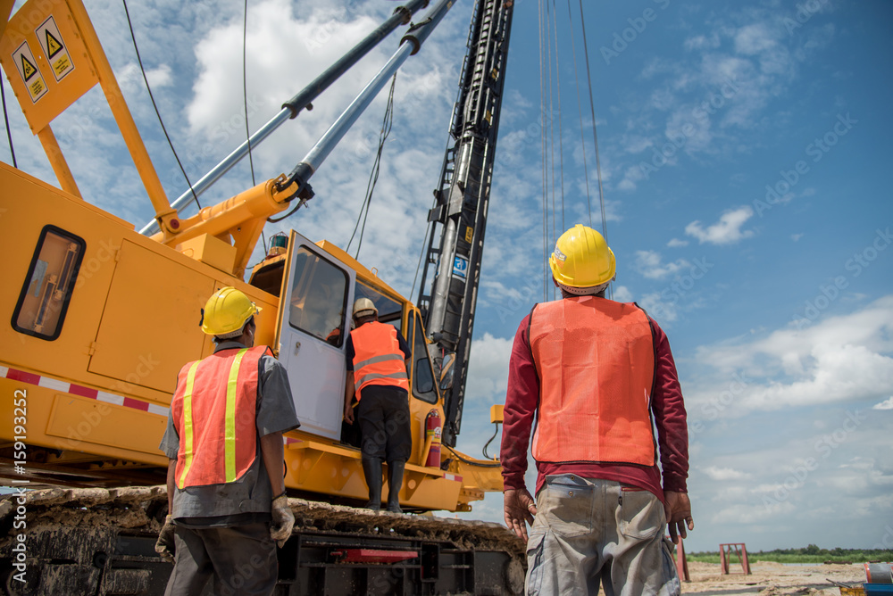 Engineer and foreman looking at heavy machine Assembly concrete pile driving truck for working against building construction crane Engineer and foreman looking at heavy machine Assembly concrete pile driving truck for working against building construction crane