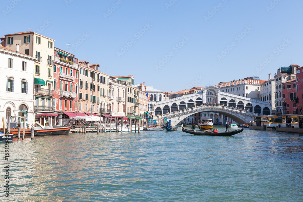 View of Rialto Bridge , Venice , Veneto, Italy from the Grand Canal with a gondola passing in front of it and reflections