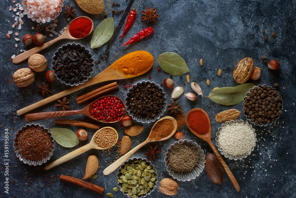 Various indian spices in wooden spoons and metal bowls, herbs and nuts on dark stone table. Colorful spices, top view,space for text. Healthy food background