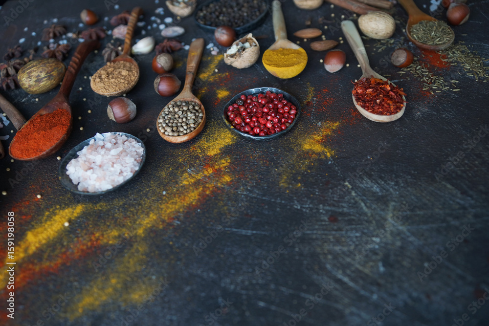 Various indian spices in wooden spoons and metal bowls, herbs and nuts on dark stone table. Colorful spices, selective focus. Healthy food background