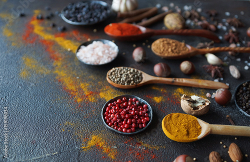 Various indian spices in wooden spoons and metal bowls, herbs and nuts on dark stone table. Colorful spices, selective focus. Healthy food background © Irina