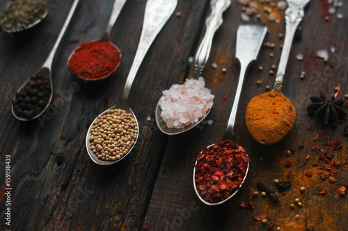 colorful spices in vintage silver spoons on rustic wooden background, selective focus 