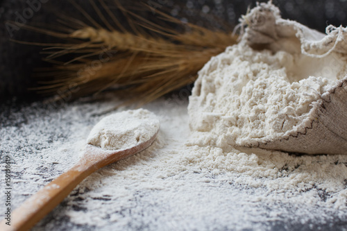 wheat flour in burlap bag, wooden spoon and ears of wheat, selective focus