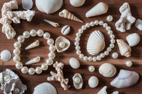Different size and shape shells and pearls spread across a wooden background