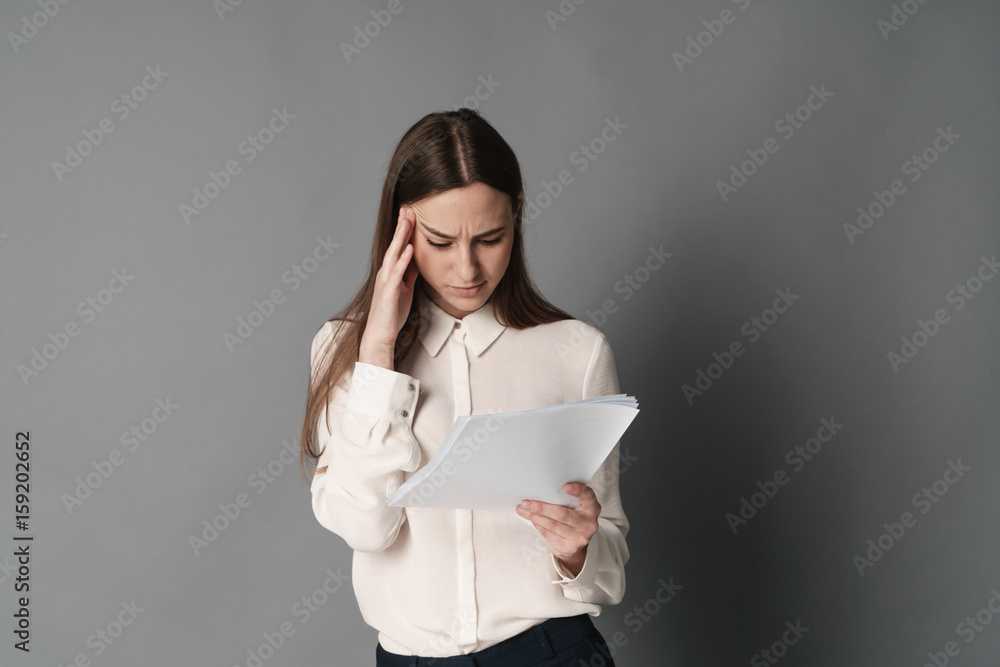 Businesswoman holding his head reading documents. Isolated on gray background. Portrait of businesswoman. Businesswoman holding his head reading documents. Isolated on gray background. Portrait of businesswoman.