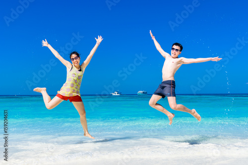 The happy Cheerful couple enjoys relaxing and jumping at white sand beach with blue sky and blue sea background.