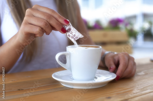 Billede på lærred Young woman adding sugar to the coffee