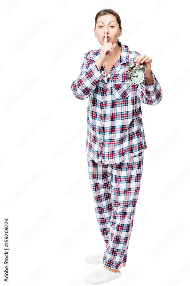 Girl with an alarm clock in checkered pajamas showing a gesture quieter on a white background Girl with an alarm clock in checkered pajamas showing a gesture quieter on a white background