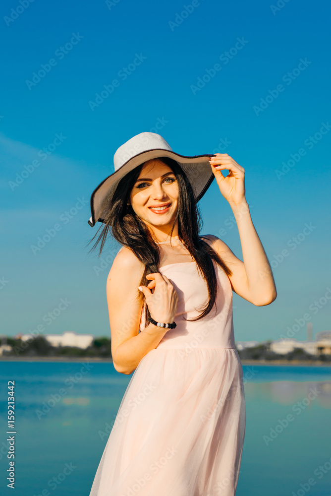 Beautiful brunette woman in  dress smiling at water and sky background
