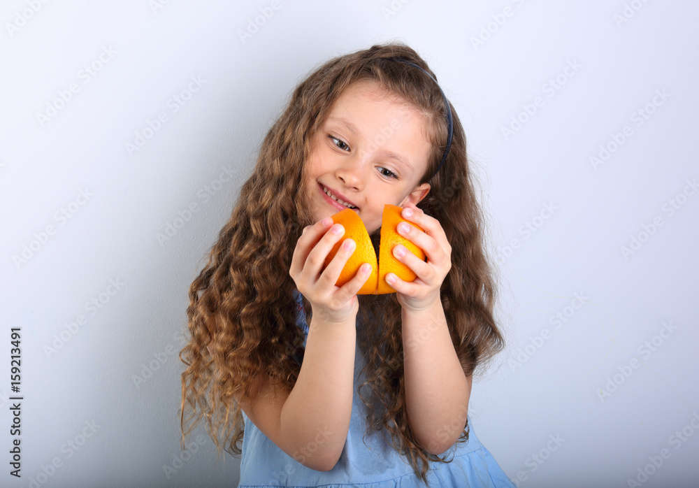 Cute smiling happy kid girl with curly hair style holding and playing citrus orange fruit slices in the hands on blue background. Cute smiling happy kid girl with curly hair style holding and playing citrus orange fruit slices in the hands on blue background.