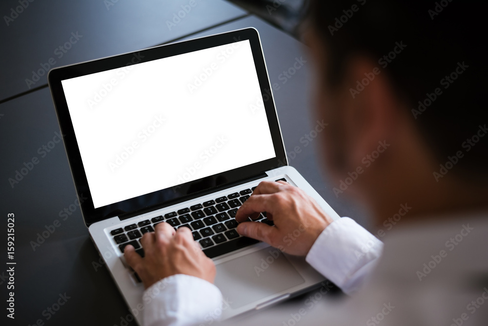 Businessman at a desk in an office typing on a laptop computer with blank white screen Businessman at a desk in an office typing on a laptop computer with blank white screen