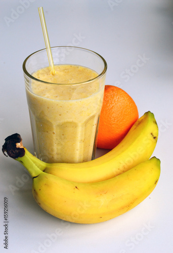 A composition of bananas and orange and a glass with smoothies